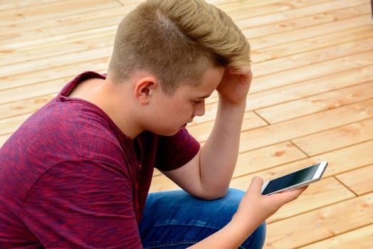 blond boy in front of wooden ground using his phone