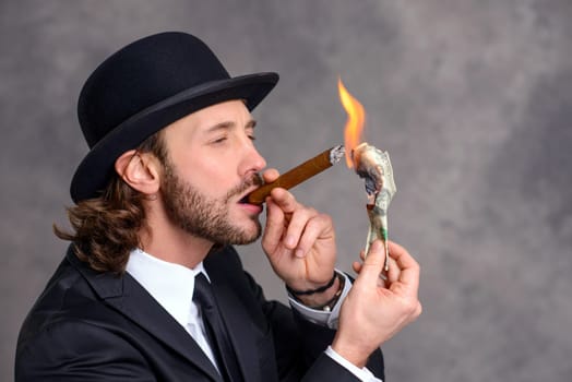 young businessman with bowler hat lighting big cigar with money