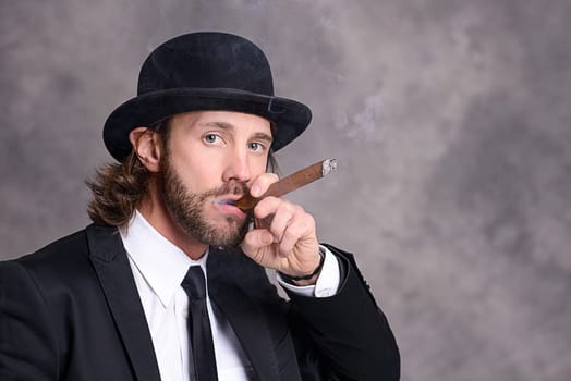 young businessman with bowler hat in black suit smoking big cigar