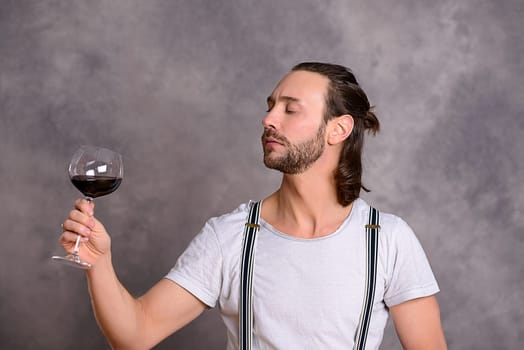 young man in front of gray background drinking red wine