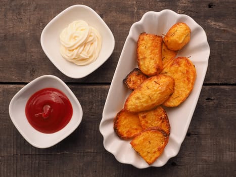 Rosemary potatoes with ketchup and mayonnaise on a wooden table