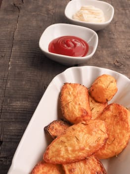 Rosemary potatoes with ketchup and mayonnaise on an old wooden kitchen table