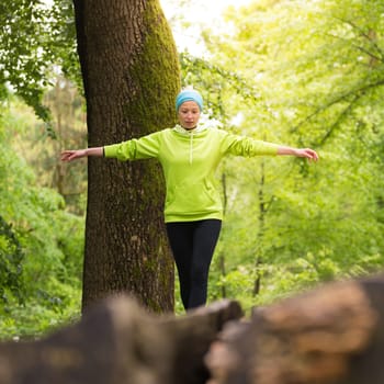 Active sporty woman holding balance on tree trunk while workout in nature. Wellness and healthy lifestyle concept.