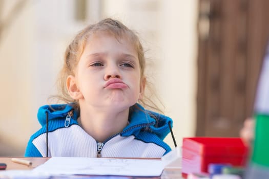 Frustrated girl sitting at a table in the courtyard of the house and looking cocky