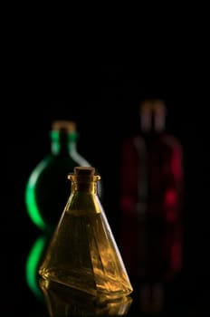 three colored decorative bottles on glass plate against a black background
