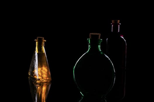 three colored decorative bottles on glass plate against a black background