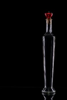 Still life of a standing narrow empty glass bottle against a black background.