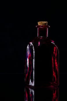 Still life of a red angular bottle with border light against a black background