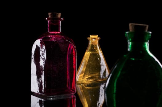 three colored decorative bottles on glass plate against a black background