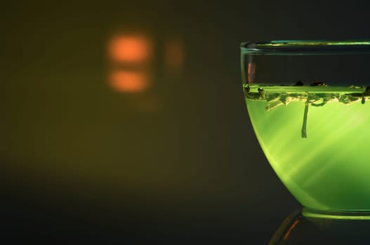 Cut close-up of a glass cup against a green illuminated background with a bright reflection.