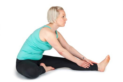 Full body view of a young blonde woman during yoga exercise "sitting in half leg and the upper body stretched to the left foot"" against a white background with a slight shadow"