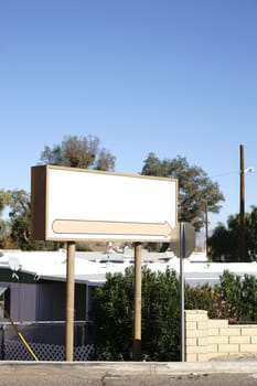 A large empty sign stands in front of the fences of a garden with gazebos.