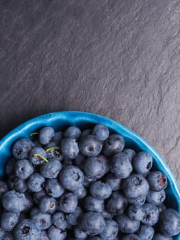 Fresh delicious blueberries in a rustic bowl on dark slate with space for text