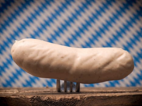 Bavarian veal sausage on a fork in front of a Bavarian flag, selective focus on the sausage
