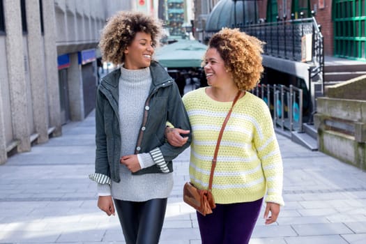 Friends walking arm-in-arm through the city. They are looking at each other and laughing.
