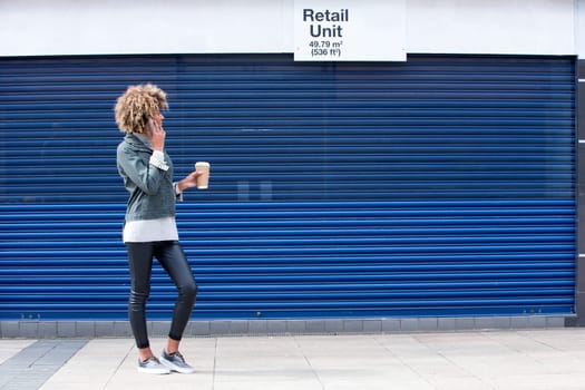 Young woman enquiring about a retail unit on the phone. She is dressed casually and is holding a disposable coffee cup.