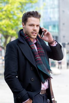 Business man in the city. He is formally dressed and is talking to someone on his smartphone.