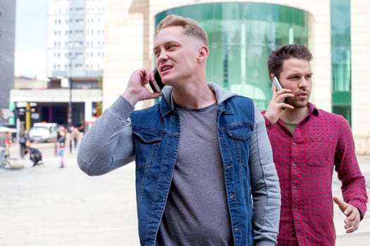Two friends on their smartphones in the city. They are both talking on the phone as they walk.