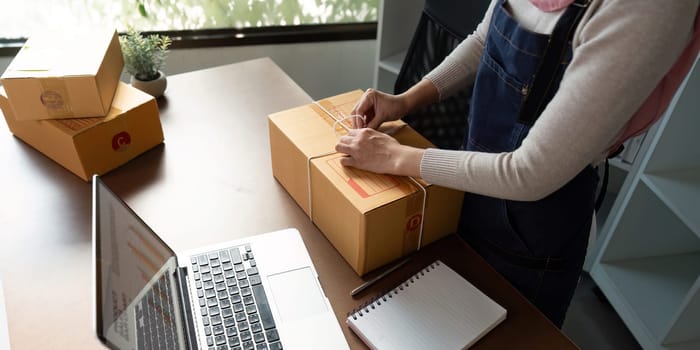 A Muslim entrepreneur seals a package for online sale, highlighting her dedication to business in a contemporary office setting.