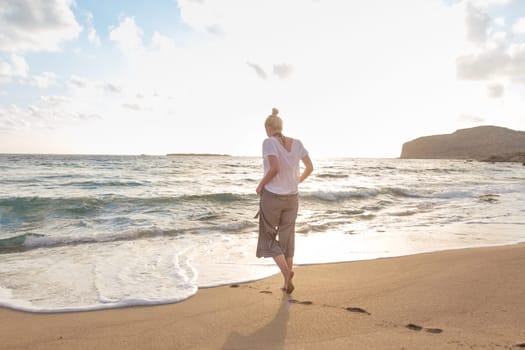 Woman walking on sand beach at golden hour. Seashore sunset walk.