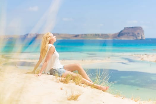 Relaxed woman enjoying sun, freedom and life an a beautiful sandy beach of Balos in Greece. Young lady feeling free, relaxed and happy. Vacations, freedom, happiness, enjoyment and well being.
