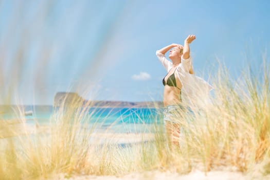 Relaxed woman enjoying sun, freedom and life an a beautiful beach. Young lady feeling free, relaxed and happy. Concept of vacations, freedom, happiness, enjoyment and well being.