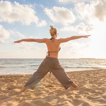Active young woman practicing yoga on beach at sunset.