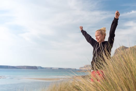Active sporty woman, arms rised, enjoying sun, freedom and life an a beautiful beach. Young lady feeling free, relaxed and happy. Active lifestyle outdoors. Made it.