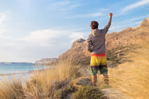 Sporty active man, arm rised, enjoying beauty of nature, freedom and life at beautiful landscape. Active lifestyle outdoors. Made it.