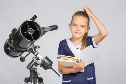Schoolgirl wondered and looked up to by reading a textbook while standing at the telescope