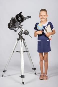Schoolgirl astronomer is a telescope with a globe and books in the hands