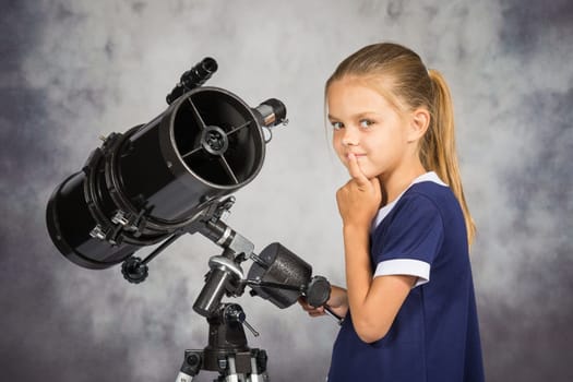 Seven-year girl thoughtfully looks in the picture, standing at the telescope