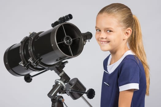 The young astronomer at the telescope is smiling and looking to the frame