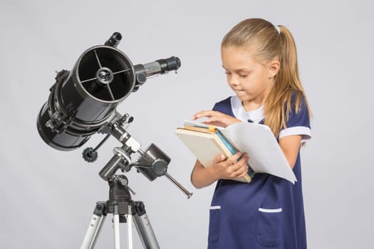 Schoolgirl astronomer leafing through books to find the right information at the stand of the telescope