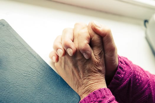 elderly women hands crossed in prayer next to Bible