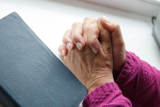 elderly women hands crossed in prayer next to Bible
