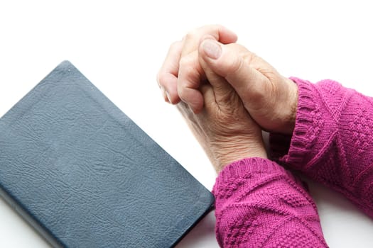 elderly women hands crossed in prayer next to Bible
