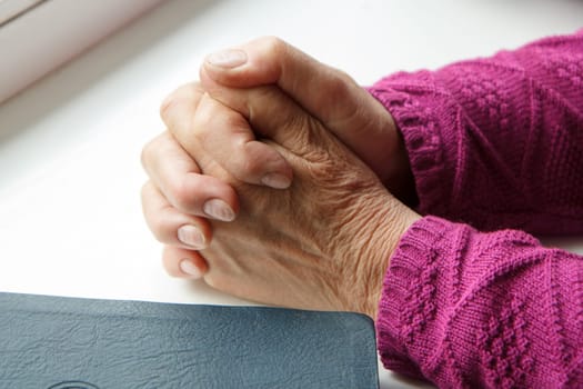 elderly women hands crossed in prayer next to Bible