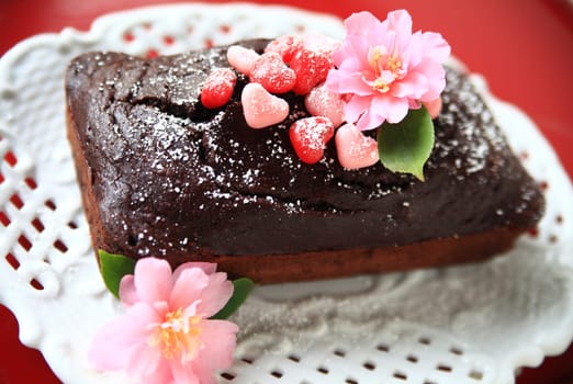 Chocolate cake with powdered sugar, heart-shaped candies and fresh flowers
