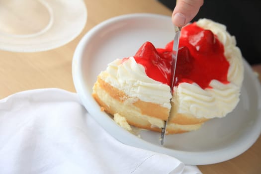A man slices a cake filled with custard, topped with whipped cream and strawberries.