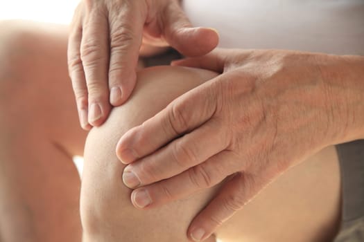 Older man puts both hands on an aching knee.