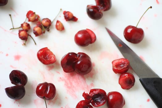 Fresh red cherries, some whole, others pitted with pile of pits and paring knife