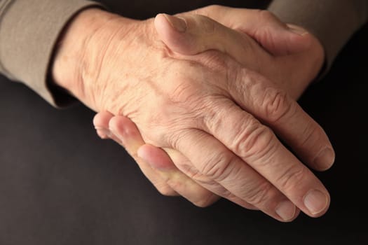 An older man grasps his hand on a black background with copy space.
