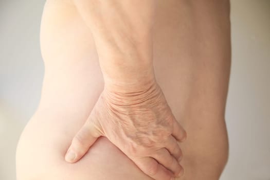 A shirtless man has his hand on his sore back.