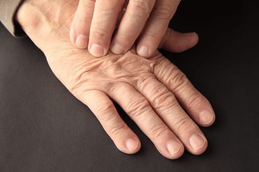 An older man has pain on his hand on a black background.