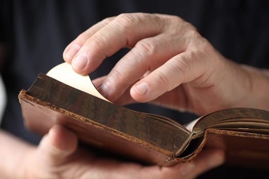 A senior man holds an antique book, and turns a page.