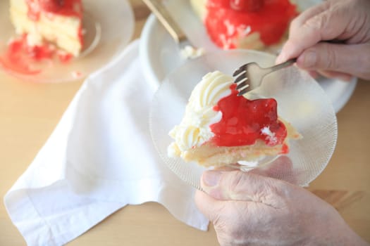Man holds glass dish with portion of cake with whipped cream and strawberry glaze.