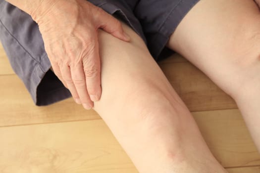 Older man sitting on the floor has a hand on his painful thigh muscle.