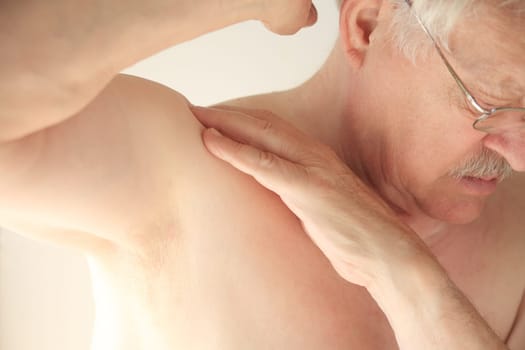 An older man tries to move his shoulder without pain.