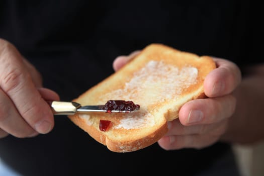 Older man spreads grape jam on a slice of buttered toast, copy space included.